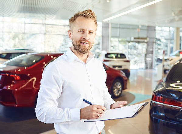 Salesman holding clipboard in showroom of Franchised Auto Dealership